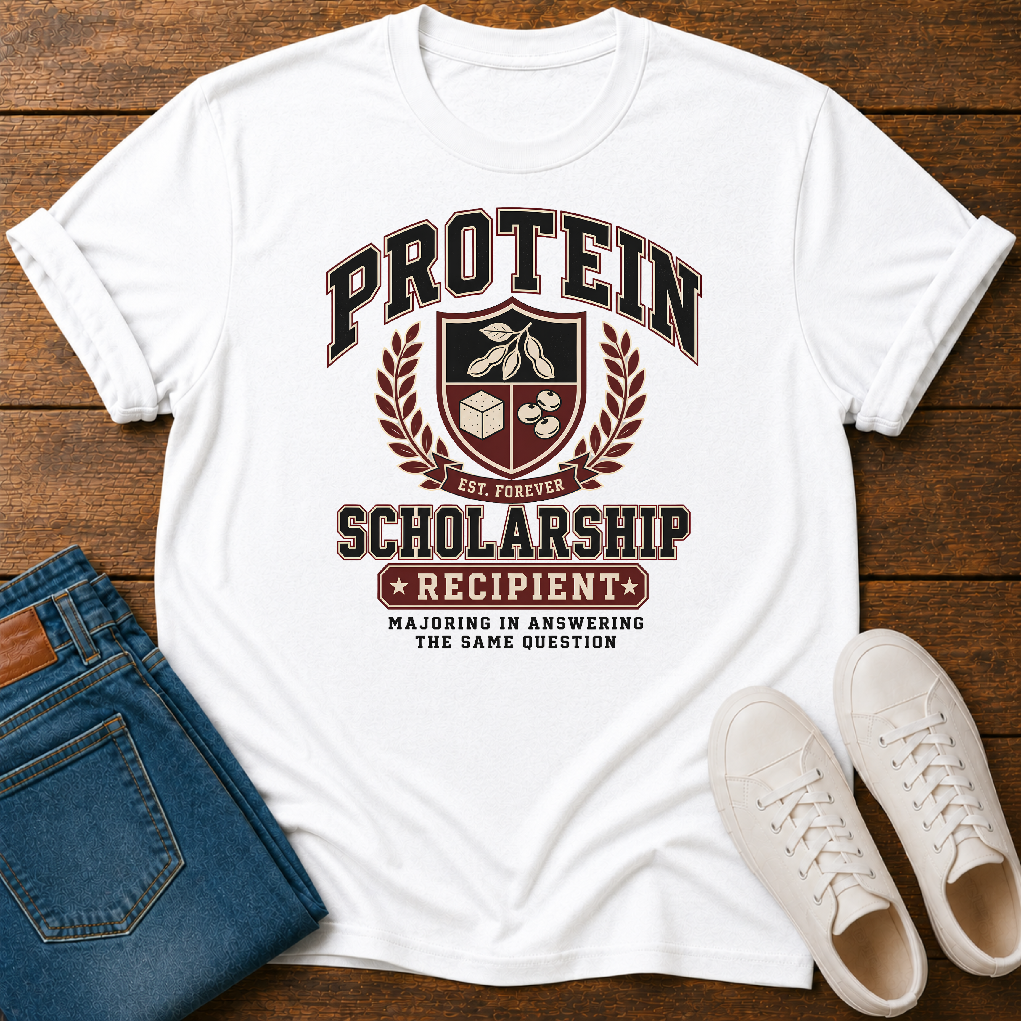 white t-shirt with Vintage collegiate crest design reading “Protein Scholarship Recipient” with soybean, tofu, and bean illustrations and the words “Majoring in Answering the Same Question.”