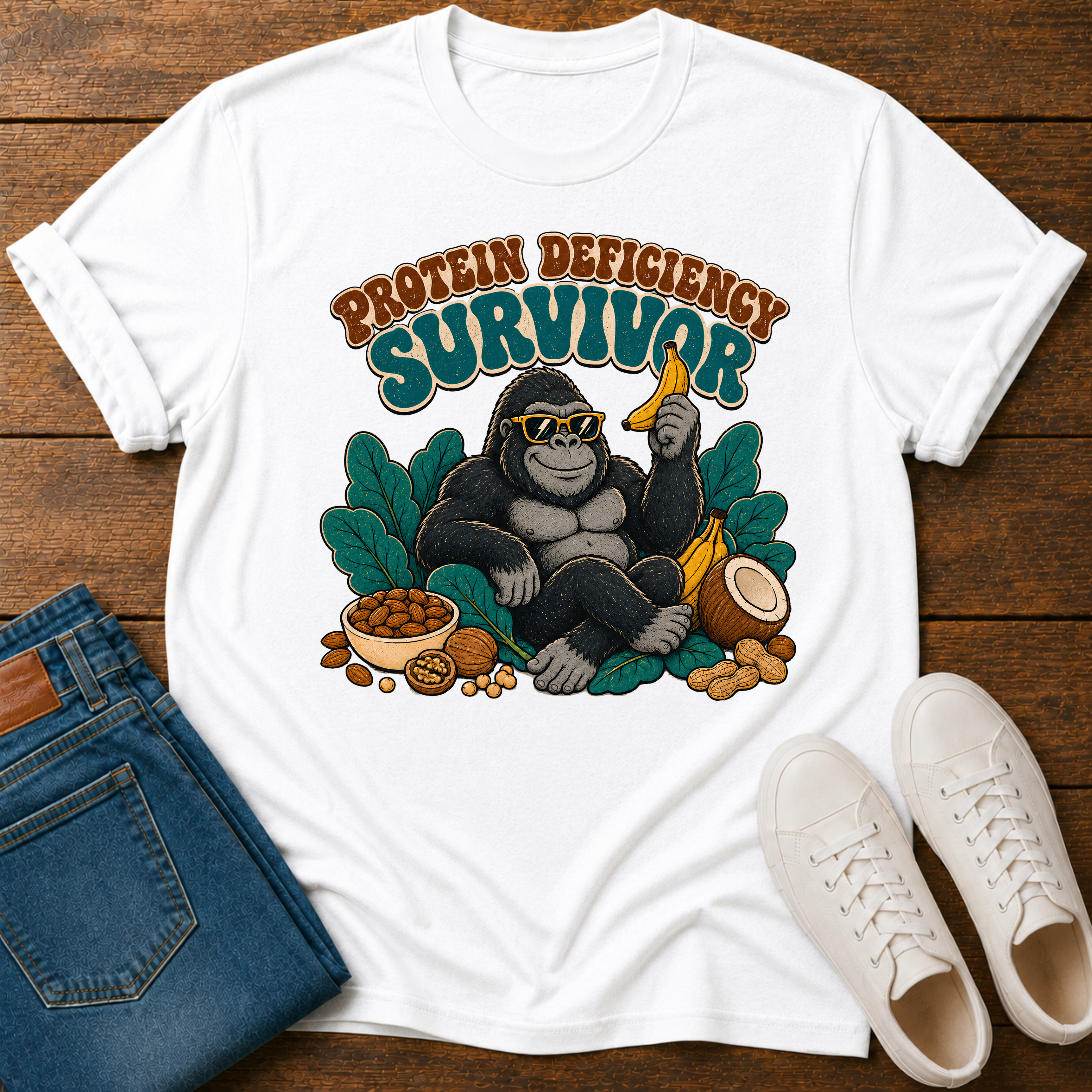 A white t-shirt with a gorilla graphic surrounded by leaves and nuts with text 'protein deficiency survivor.'