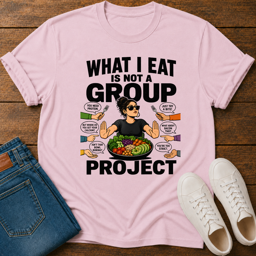 Pink t-shirt with a graphic of a woman eating salad and non vegan questions being thrown at her with text 'what i eat is not a group project" on a wooden board with jeans and sneakers