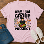 Pink t-shirt with a graphic of a woman eating salad and non vegan questions being thrown at her with text 'what i eat is not a group project" on a wooden board with jeans and sneakers