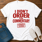 White t-shirt with red text 'i didn't order the commentary comments closed' on a wooden surface with jeans and sneakers. 